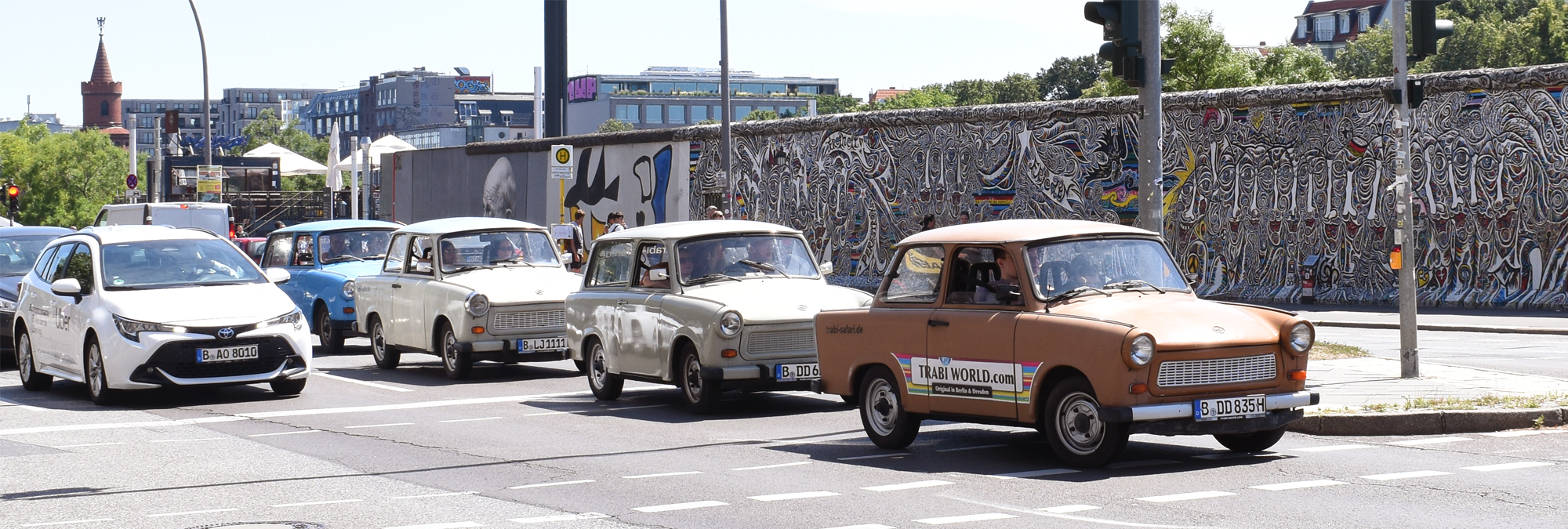 Vintage Trabant cars driving past the East Side Gallery section of the Berlin Wall covered in murals and street art.