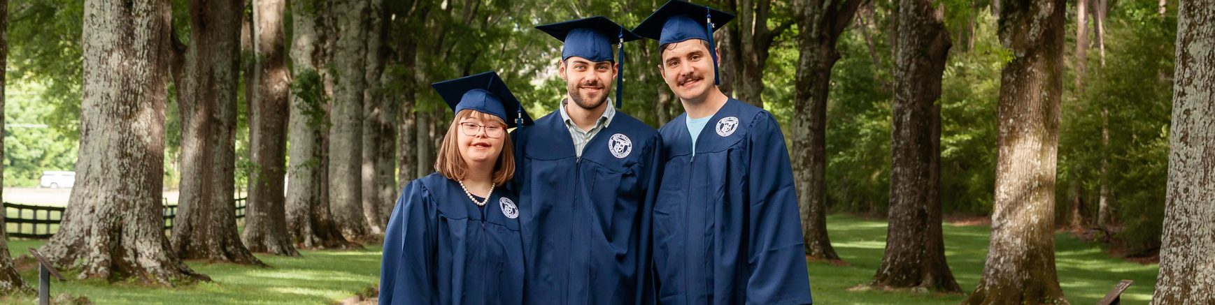 Three IPSE graduates standing together in the middle of the road, with trees lining up and down on either side.