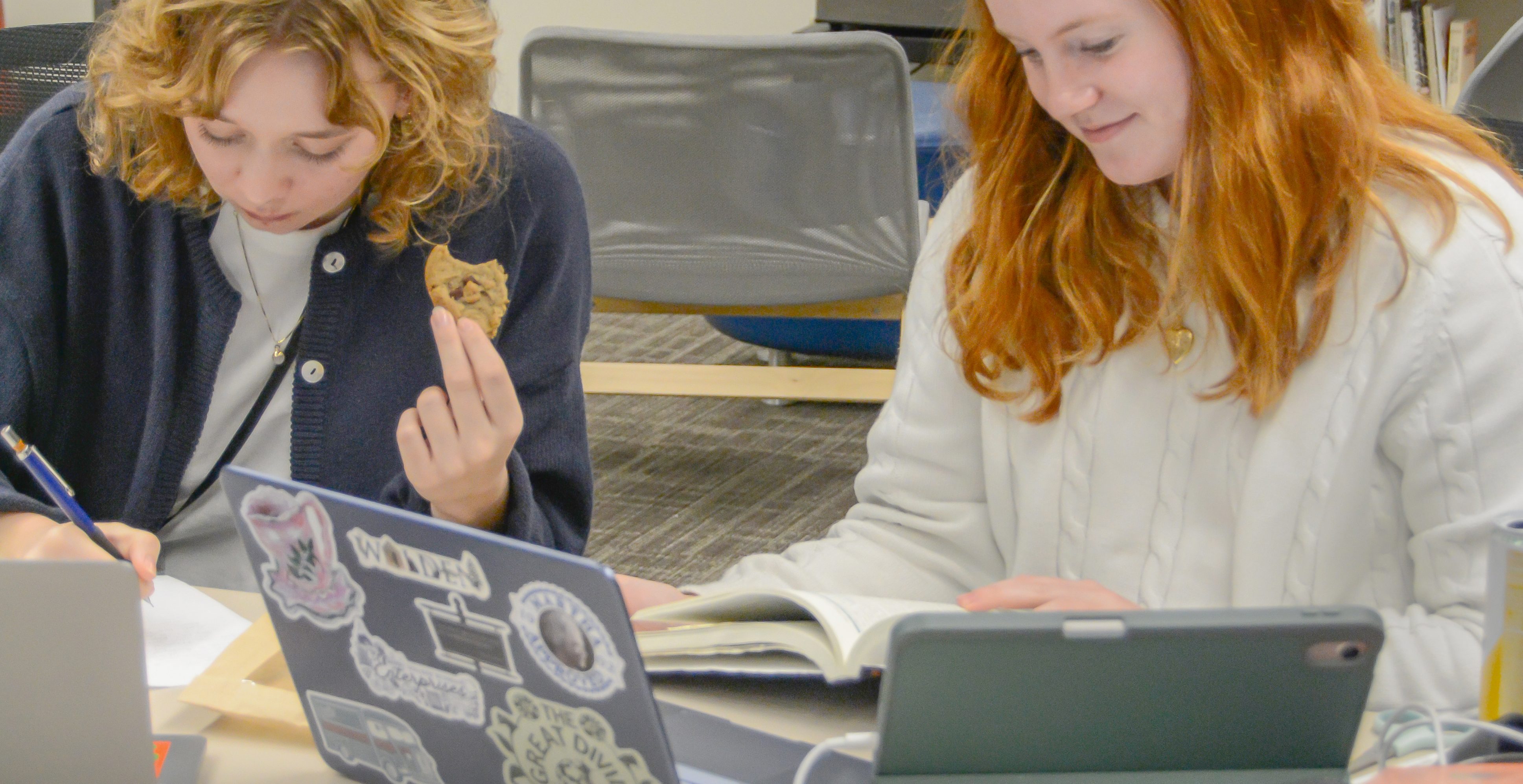 Two Berry students sitting at a table, with both of them working on assignments; various papers, books, and electronics cover the table.